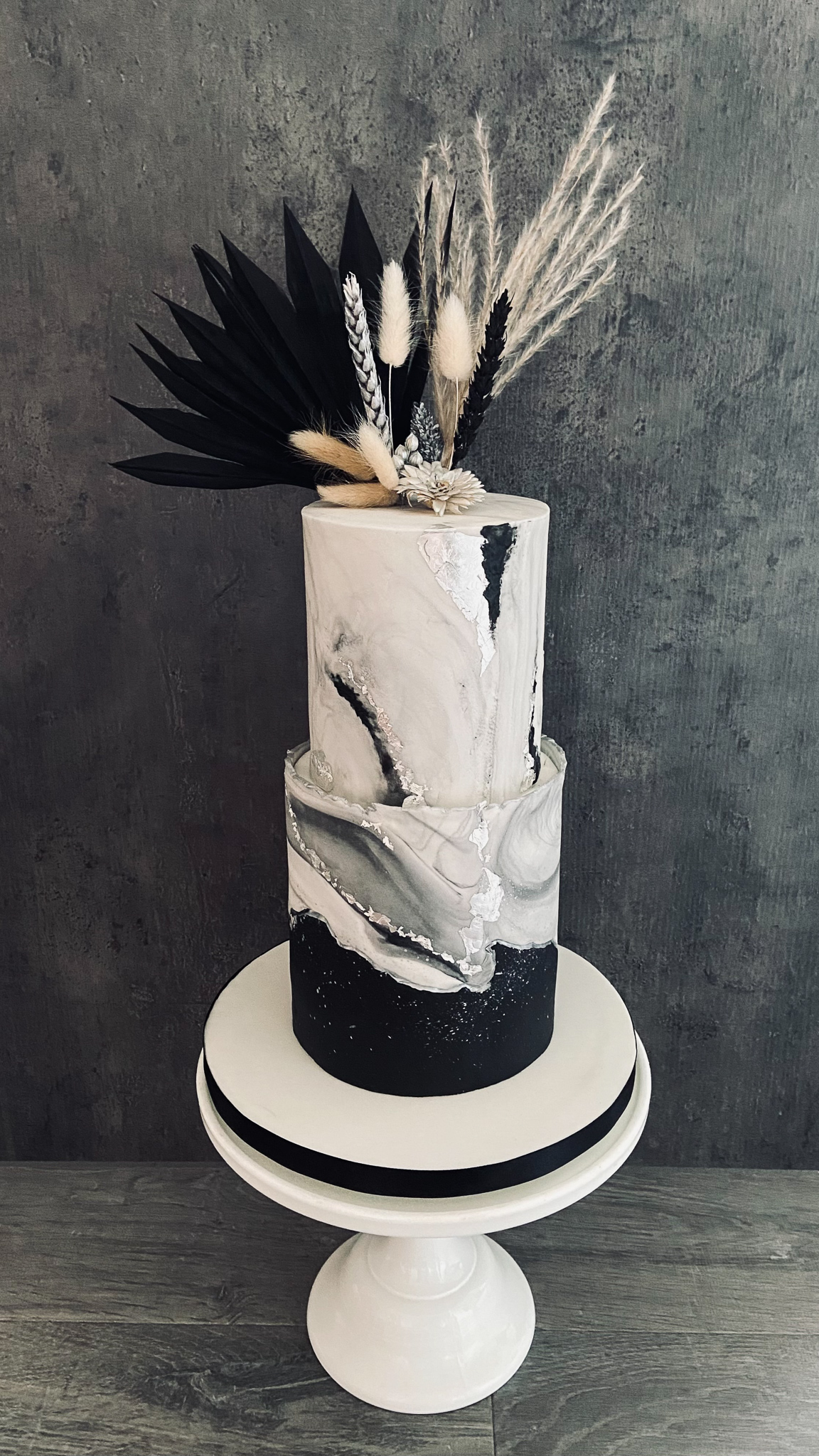 Stylish black and white textured marble cake with silver leaf and dried flowers